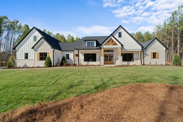 A large modern farmhouse with a spacious lawn under a blue sky.