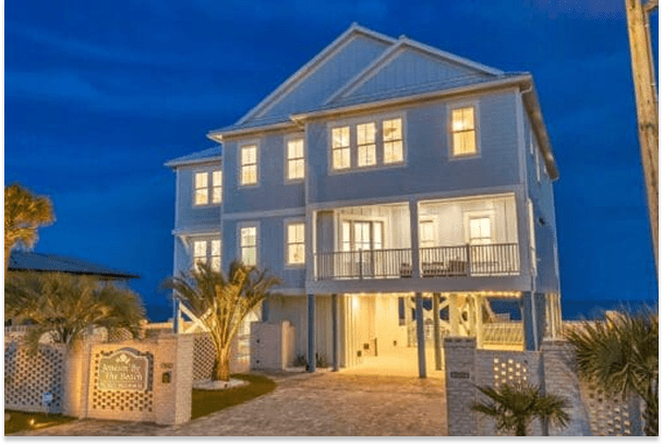 Large modern beach house illuminated at night with palm trees.