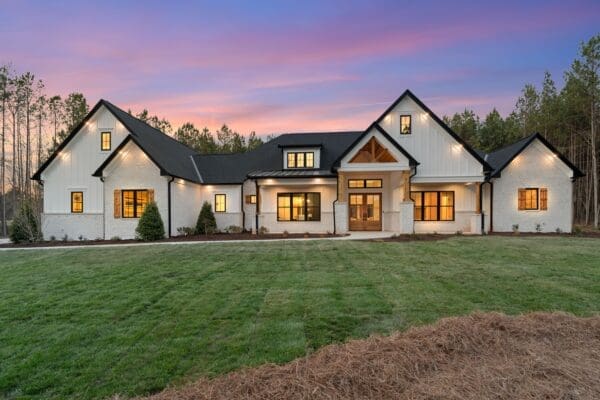Modern farmhouse with large windows and warm lighting at dusk.