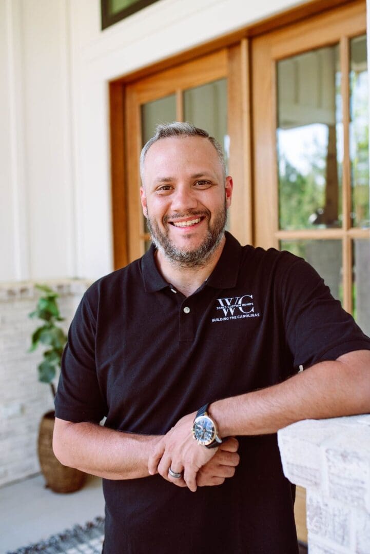 Smiling man in a black polo shirt standing outdoors.