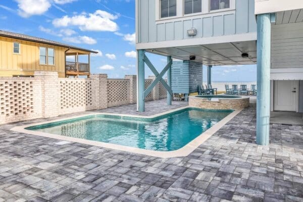 Modern outdoor pool area under a raised beach house with stone pavers.