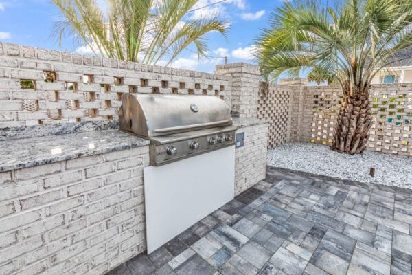 Modern outdoor barbecue grill area with stone walls and palm trees.