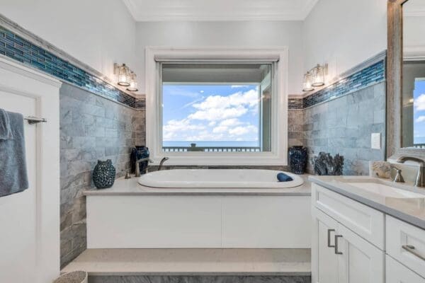 Modern bathroom with a large bathtub under a window showing a blue sky.