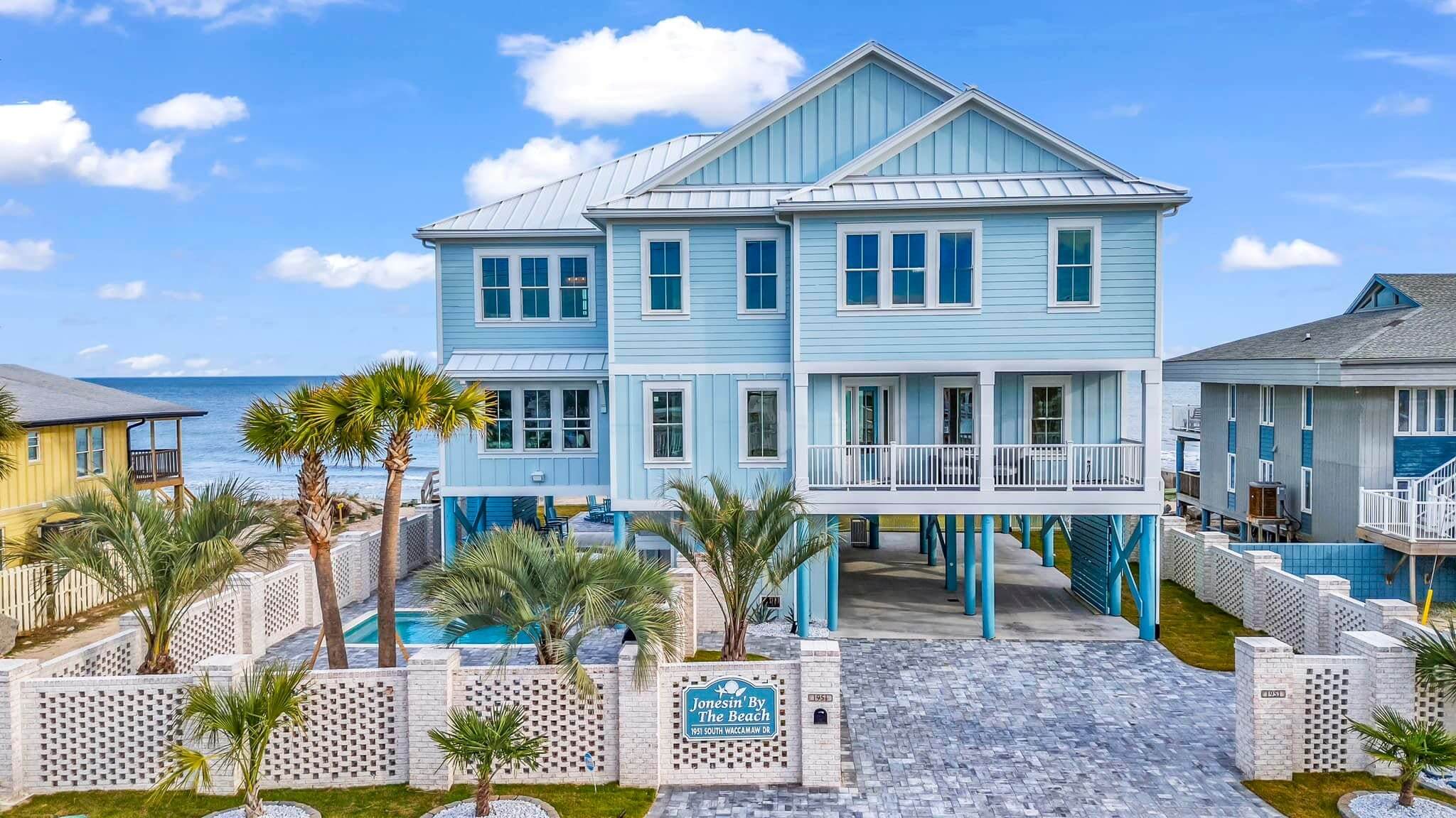 Coastal blue beach house elevated on stilts with palm trees.